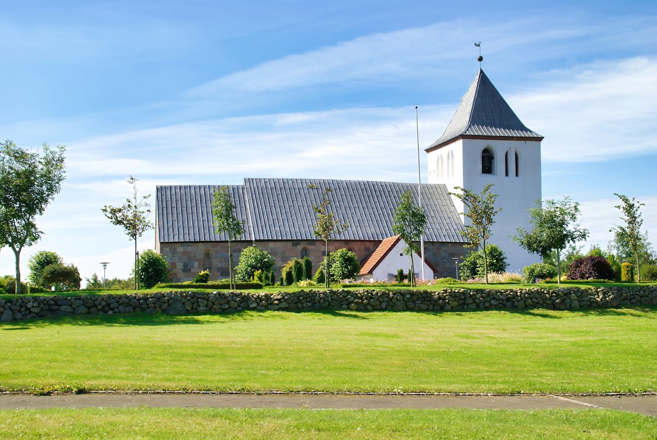 Beautiful view of Mabjerg Church in Denmark, surrounded by lush greenery and clear blue skies.